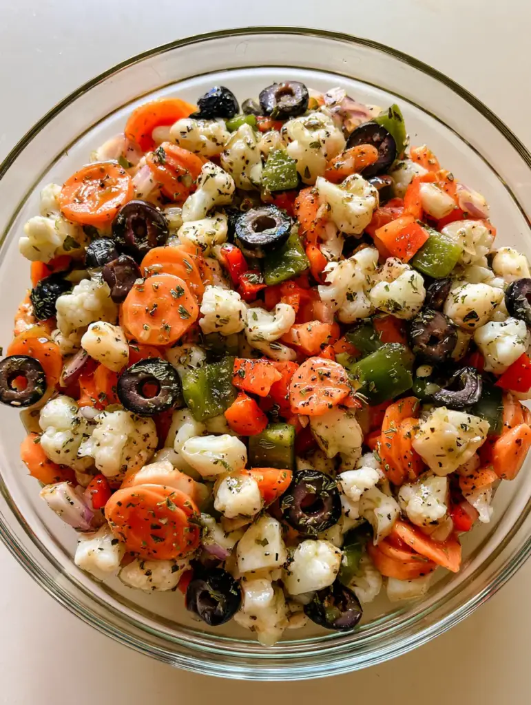 Close up of the colorful textures in a Marinated Cauliflower Salad featuring orange carrot circles and black olive rings.