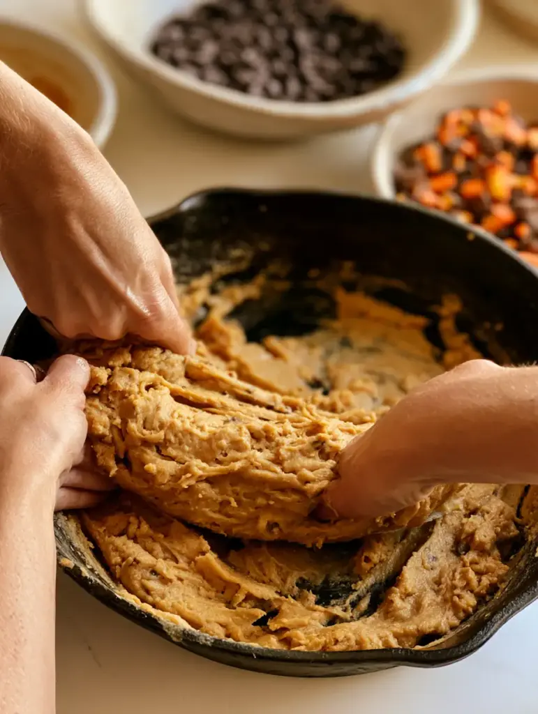 A slice of Peanut Butter Chocolate Chip Cookie Pizza being lifted to show a chocolate cheese-pull.