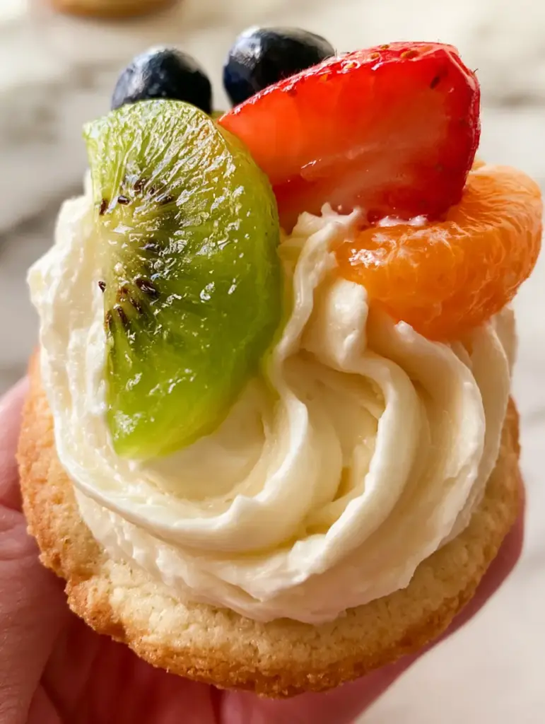 Detailed view of the velvety cream cheese frosting swirl on a Mini Fruit Pizza, topped with a fresh strawberry half and mandarin segment.