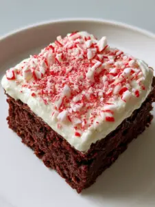 Close-up high-angle shot of a dense dark chocolate Peppermint Brownie with thick white frosting and crushed candy canes. (Peppermint Brownies)