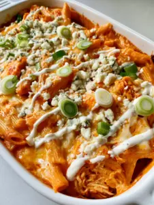 A close-up handheld smartphone photo of creamy Buffalo Chicken Pasta in a white dish, showing vibrant orange sauce and melted mozzarella.