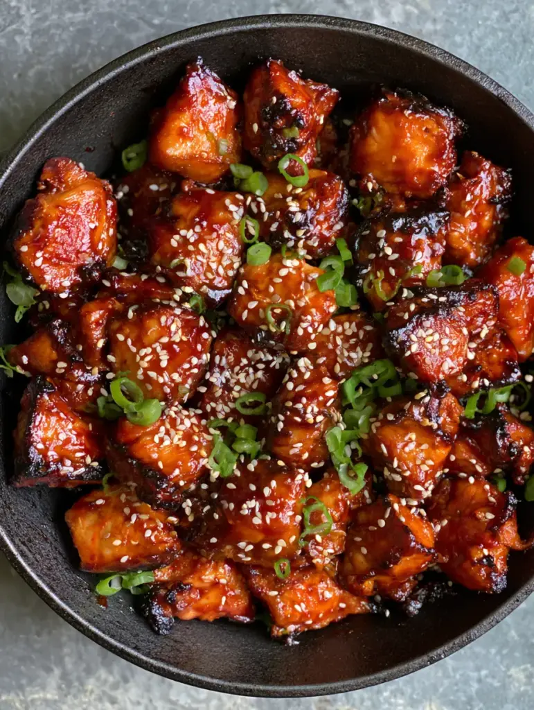 Korean Gochujang Chicken: The Ultimate Glossy and Spicy Skillet Dinner 2 Top-down view of charred Korean Gochujang Chicken pieces in a black skillet with vibrant red sauce and green onions.