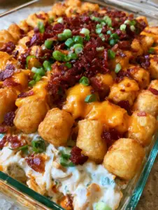 A close-up shot of golden-brown tater tots topped with melted orange cheddar and dark bacon crumbles. (Chicken Bacon Ranch Tater Tot Casserole)