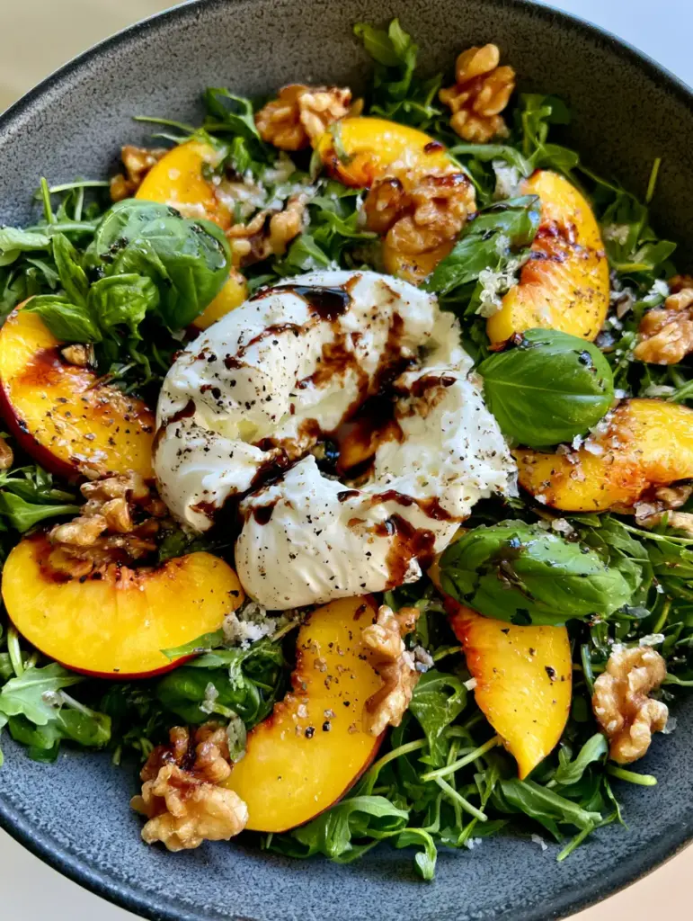 Toasted walnuts and fresh basil leaves garnishing a summer peach salad with flaky sea salt.