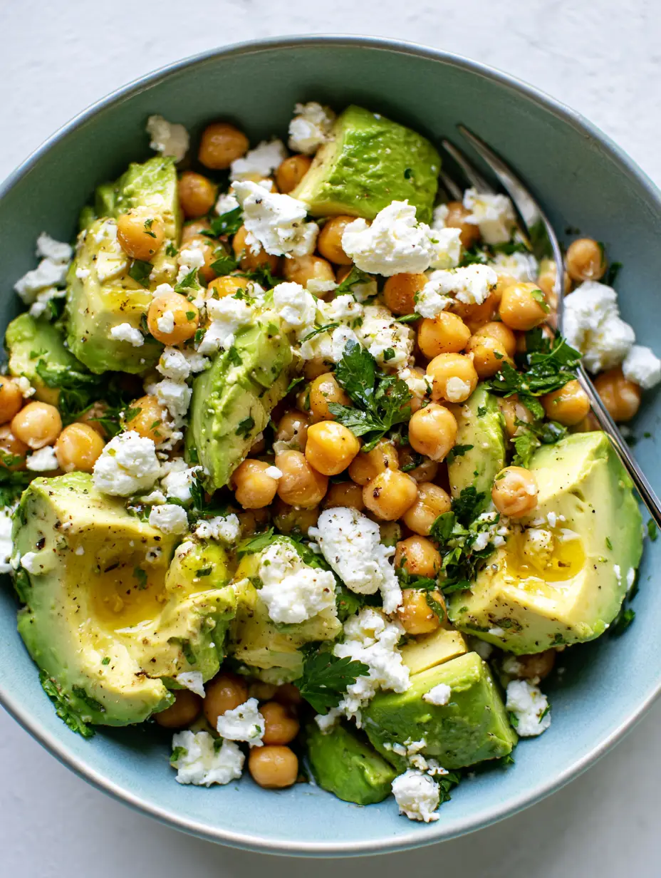 Close-up of golden chickpeas and snowy white feta crumbles in a chickpea feta avocado salad glistening with lemon vinaigrette.