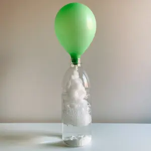 Side view of a Baking Soda Balloon Experiment showing vigorous white effervescent bubbles and a clear bottle on a white surface.