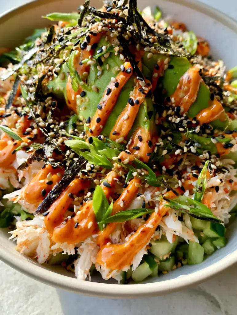 A meticulous zigzag pattern of sriracha mayo over avocado and sesame seeds. (california roll cucumber salad)