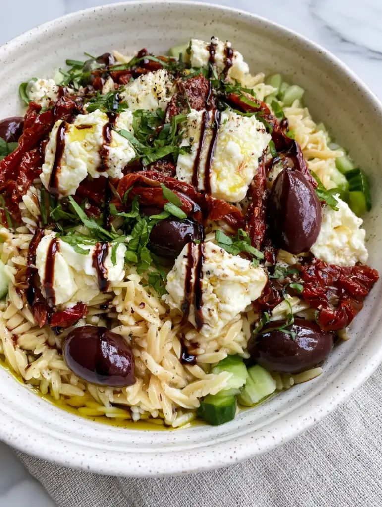 High angle view of balsamic orzo salad showing the thick dark glaze drizzles and creamy feta chunks.