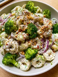Top-down view of Creamy Tortellini Broccoli Salad with fresh dill and red onion slivers in a matte white bowl.