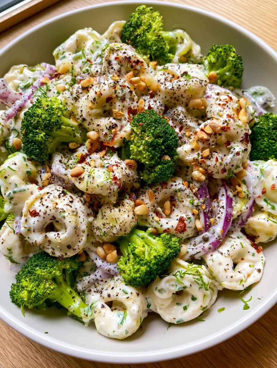 Top-down view of Creamy Tortellini Broccoli Salad with fresh dill and red onion slivers in a matte white bowl.