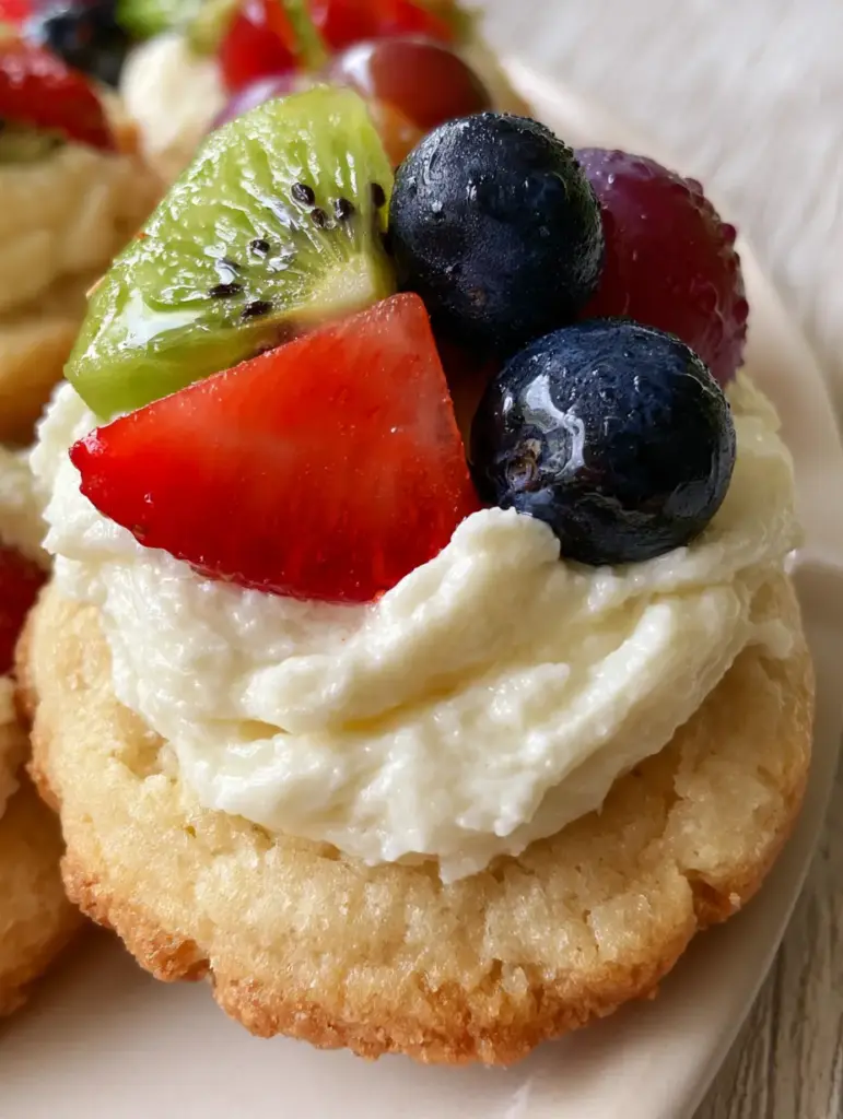 A platter of Mini Fruit Pizzas arranged like a mosaic with vibrant green kiwi and red strawberries in soft natural sunlight.