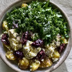 Close-up of Greek potato salad showing glistening lemon vinaigrette, rustic feta chunks, and fresh dill forest.