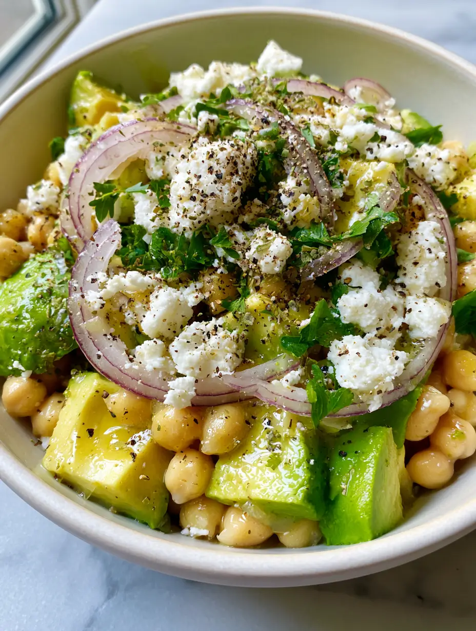 Vibrant golden chickpeas mixed with bright green avocado and snowy white feta cheese crumbles in a minimalist bowl. (chickpea feta avocado salad)