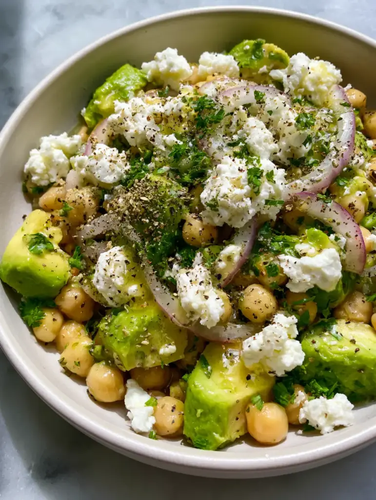 Close-up of translucent red onion arcs and emerald green parsley garnishing a glossy chickpea salad.
