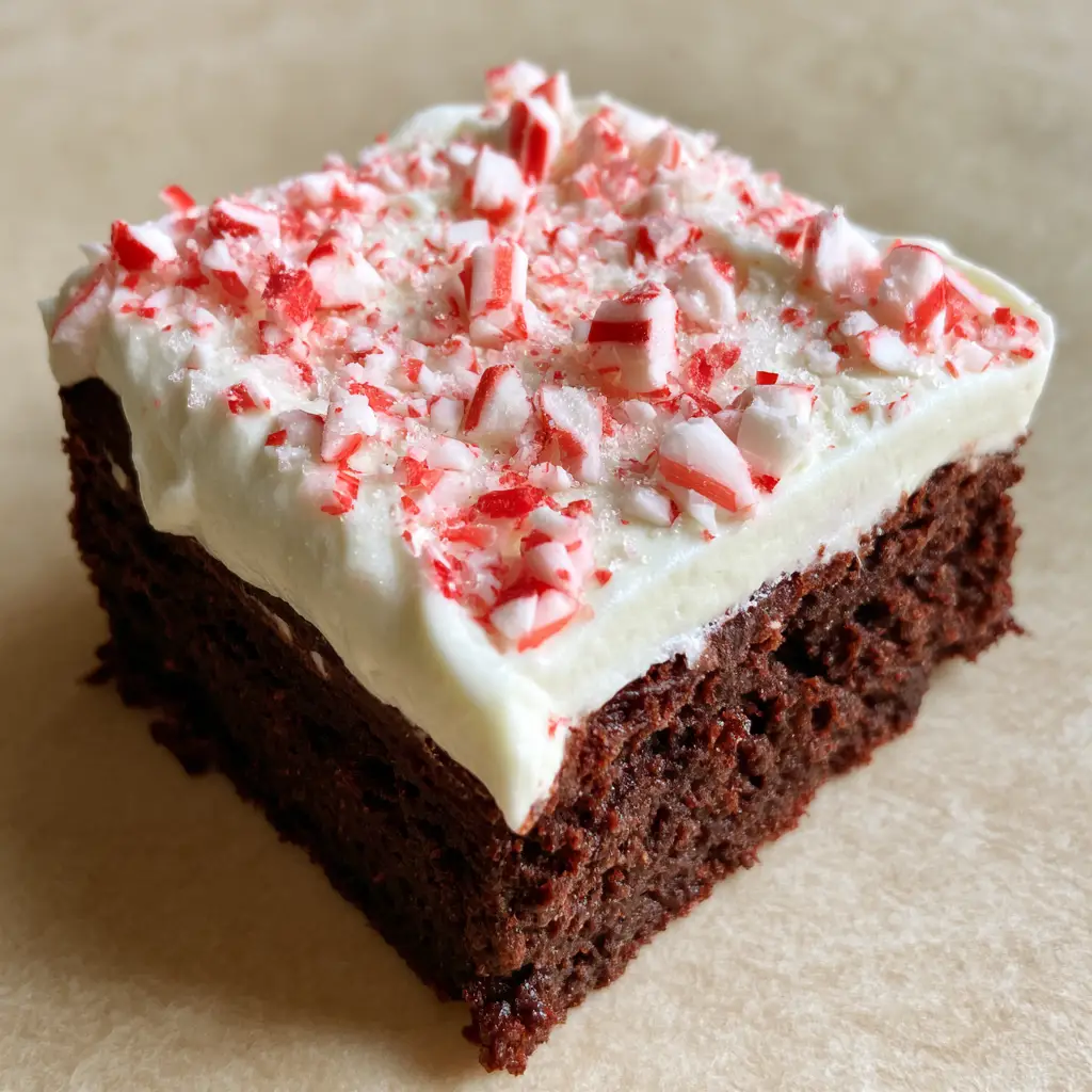 Christmas Brownie Recipes: Fudgy Peppermint Cream Brownies 1 A square peppermint brownie held up against a neutral beige background in soft daylight. (Christmas Brownie Recipes)