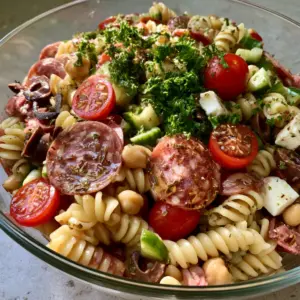 A clear glass bowl filled with High-Protein Italian Pasta Salad featuring rotini, salami, chickpeas, and feta on a grey countertop.