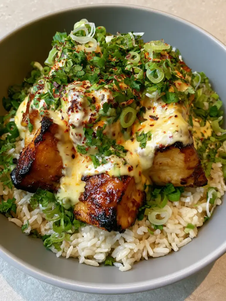 Coconut Chicken Rice Bowl: The Ultimate Creamy and Charred Weeknight Dinner 1 A thick, pale-yellow glossy coconut cream sauce being drizzled over seared chicken in a matte-grey bowl.