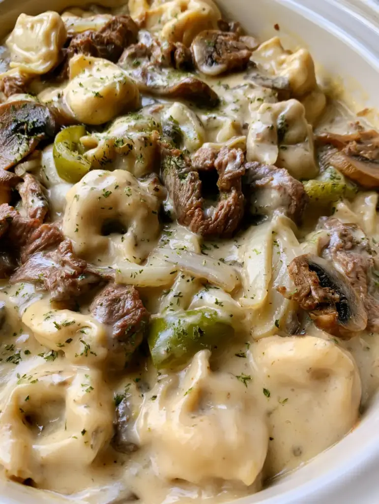 Steaming bowl of Crock Pot Cheesesteak Tortellini with visible green peppers and sautéed mushrooms.