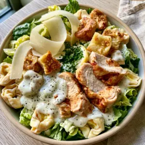 Close up of creamy tortellini Caesar salad with glossy dressing and black pepper specks. (tortellini Caesar salad)