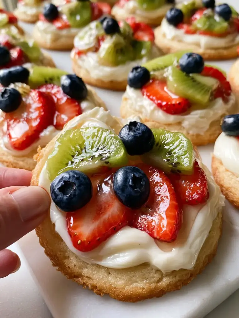 A dozen Mini Fruit Pizzas arranged on a clean white marble slab showing vibrant strawberries, blueberries, and kiwi.