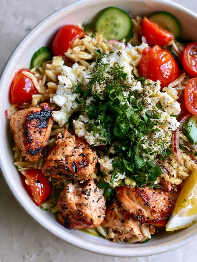 Close-up of Mediterranean Grilled Chicken Orzo Salad with glistening lemon vinaigrette and charred chicken chunks.